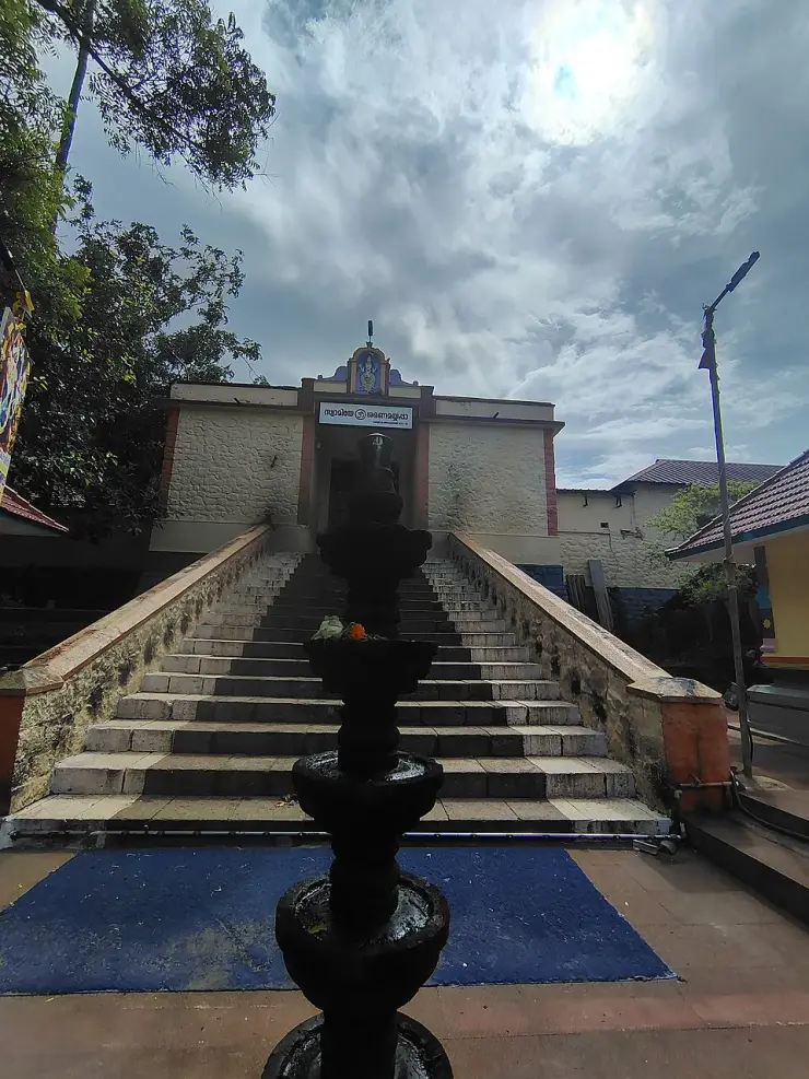 The temple steps seen head-on with a tall black stone lamp-post silhouetted in front, and the shrine entrance and its Malayalam signboard above