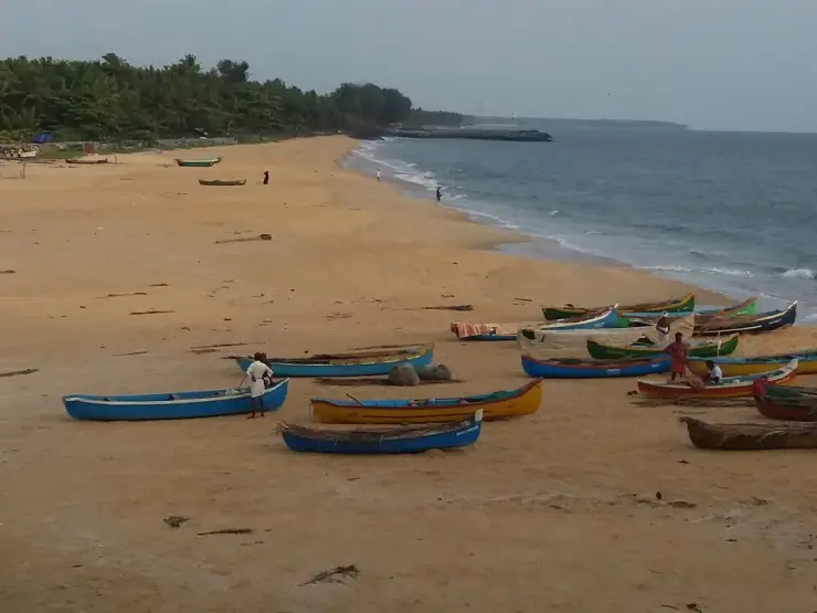 Wooden fishing canoes drawn up on the wide tan sand at Kappad, the shoreline curving away to a low rocky headland under an overcast sky.
