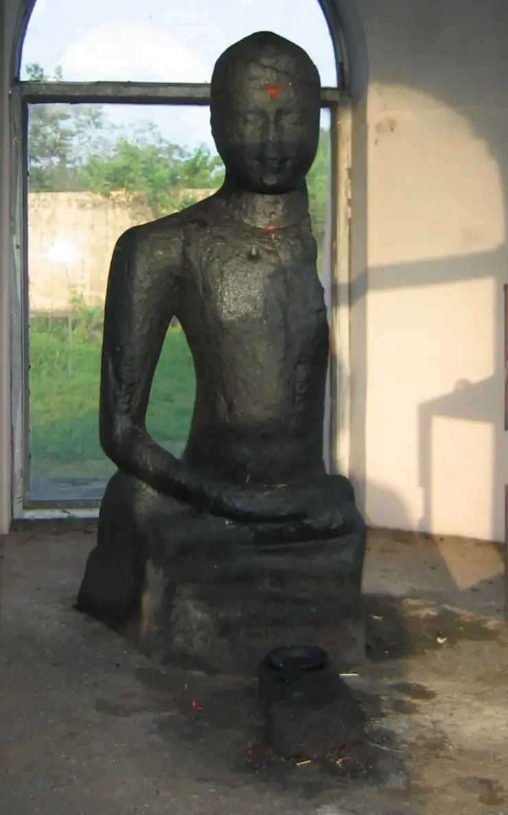 The black granite Karumadikuttan Buddha seen inside its shrine, the left arm and part of the left side missing, with red kumkumam marks on the forehead and throat
