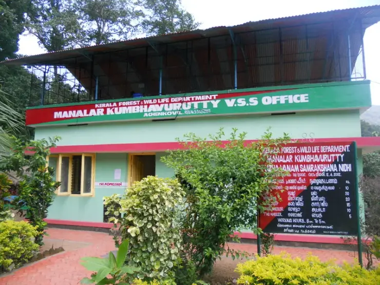 A small green and red building signed Manalar Kumbhavurutty V.S.S Office, Achenkovil, with a hand-painted tariff board on a post beside it.