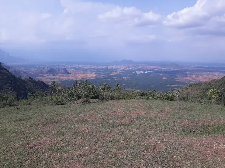 Cropped grass and red earth on the Ramakkalmedu ridge with the farmed Tamil Nadu plain and a distant peak beyond