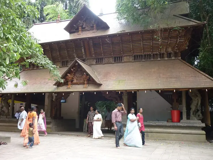 The carved timber gable and latticed clerestory of the Mannarasala temple frontage, with stone guardian figures at the corners