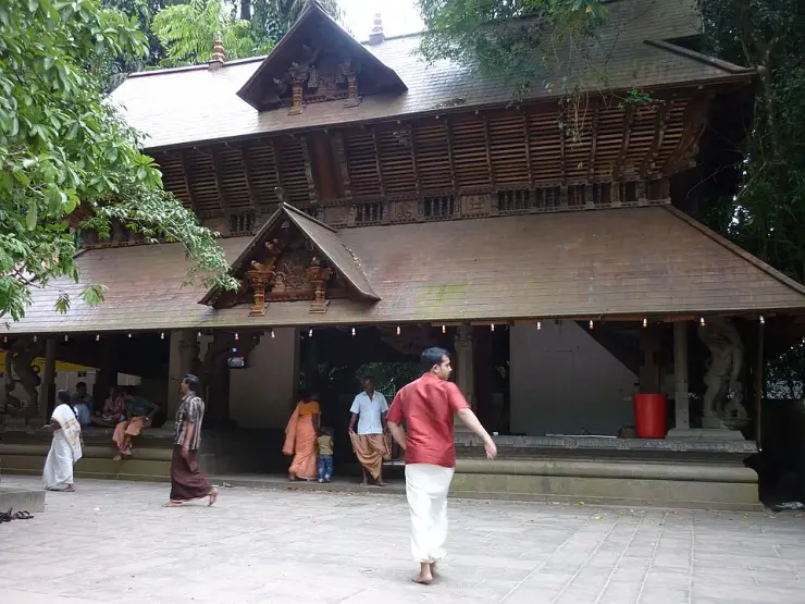The Mannarasala temple frontage with its deep tiled eaves and carved gable, worshippers crossing the paved forecourt