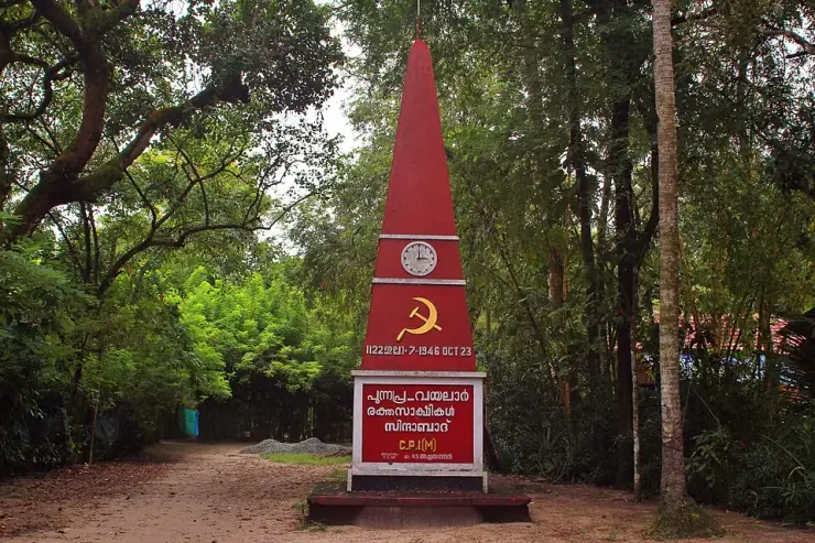 A red CPI(M) obelisk at Punnapra with a clock face, a hammer and sickle, and the date 1946 OCT 23 cast into it