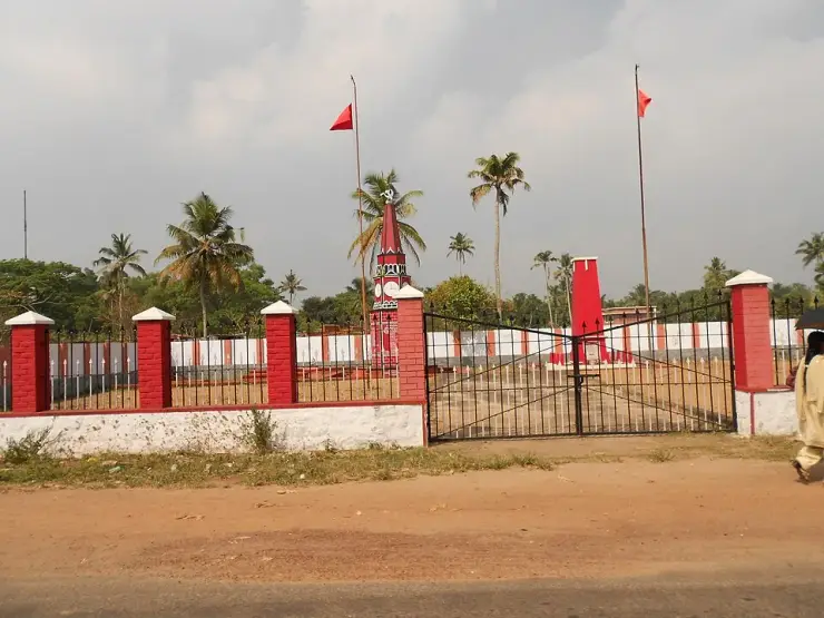 The gated enclosure of the Punnapra Vayalar Rakthasakshi Mandapam seen from the road, with red flags flying