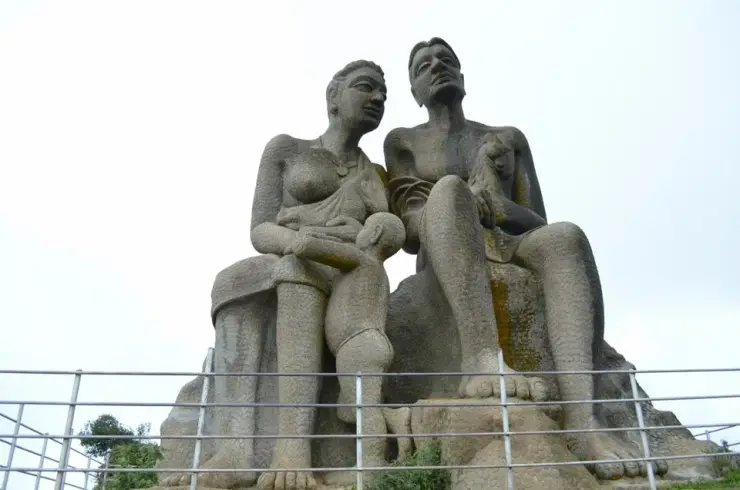 The Kuravan and Kurathi statue at Ramakkalmedu seen from below the railing, the seated tribal figures against an open sky