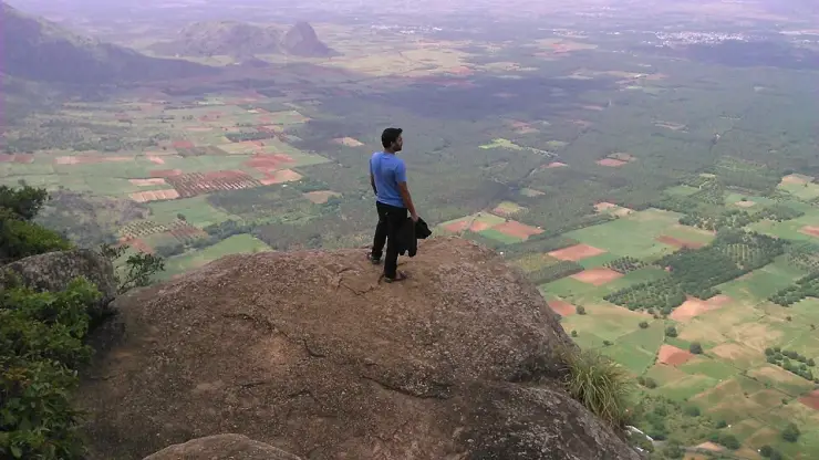 A visitor standing on bare rock at the edge of the Ramakkalmedu escarpment above the farmed Tamil Nadu plain