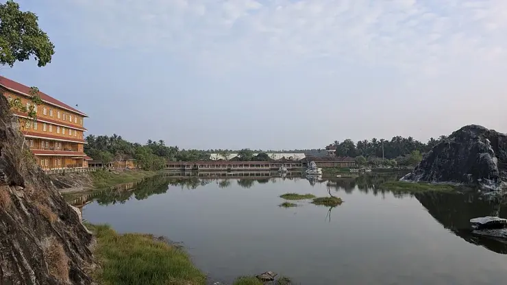 The quarry lake at Sargaalaya, Iringal, with the laterite guest-house block on the left, the long craft-hut row across the water and cut rock rising on the right