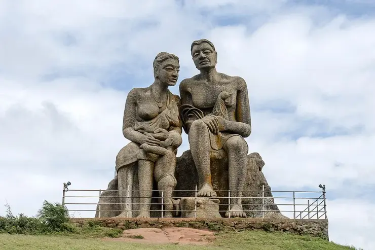 The Kuravan and Kurathi statue at Ramakkalmedu seen from the front, two seated figures on a stone plinth behind a steel guard rail