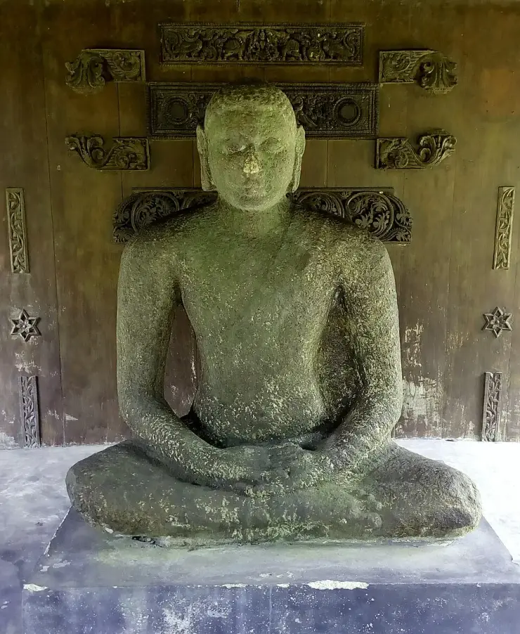 A complete seated stone Buddha in dhyana mudra at Krishnapuram Palace, displayed against a carved timber panelled backdrop
