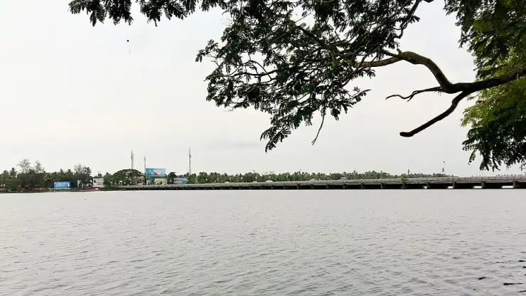 The Thottappally spillway seen across the water, its shutter line running the full width of the frame beneath a pale sky
