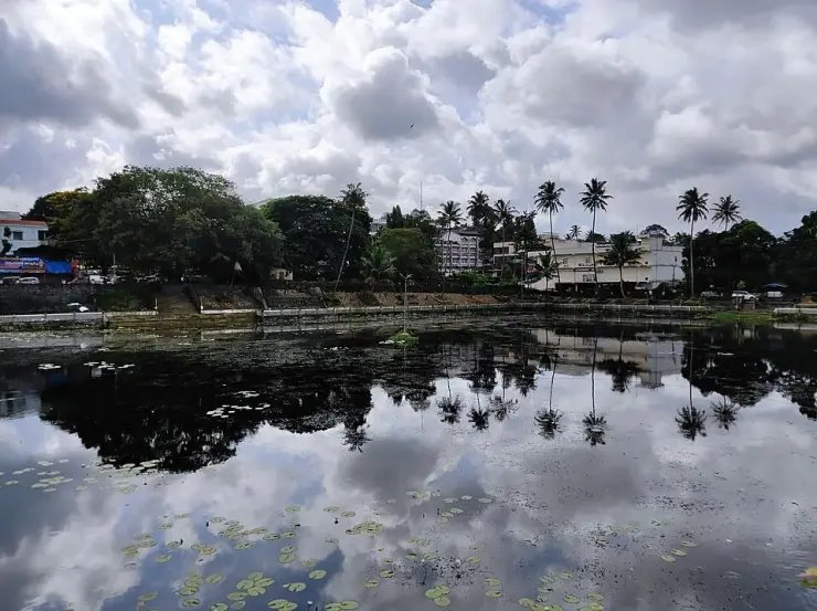 The temple tank at Kottarakkara, a broad sheet of still water edged with laterite steps and retaining walls, with the tiled temple roofs and trees behind it