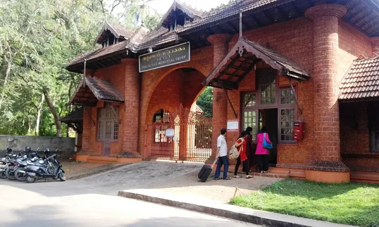 A laterite building with a tiled roof and signage inside the Thunchan Memorial grounds, with visitors at the entrance