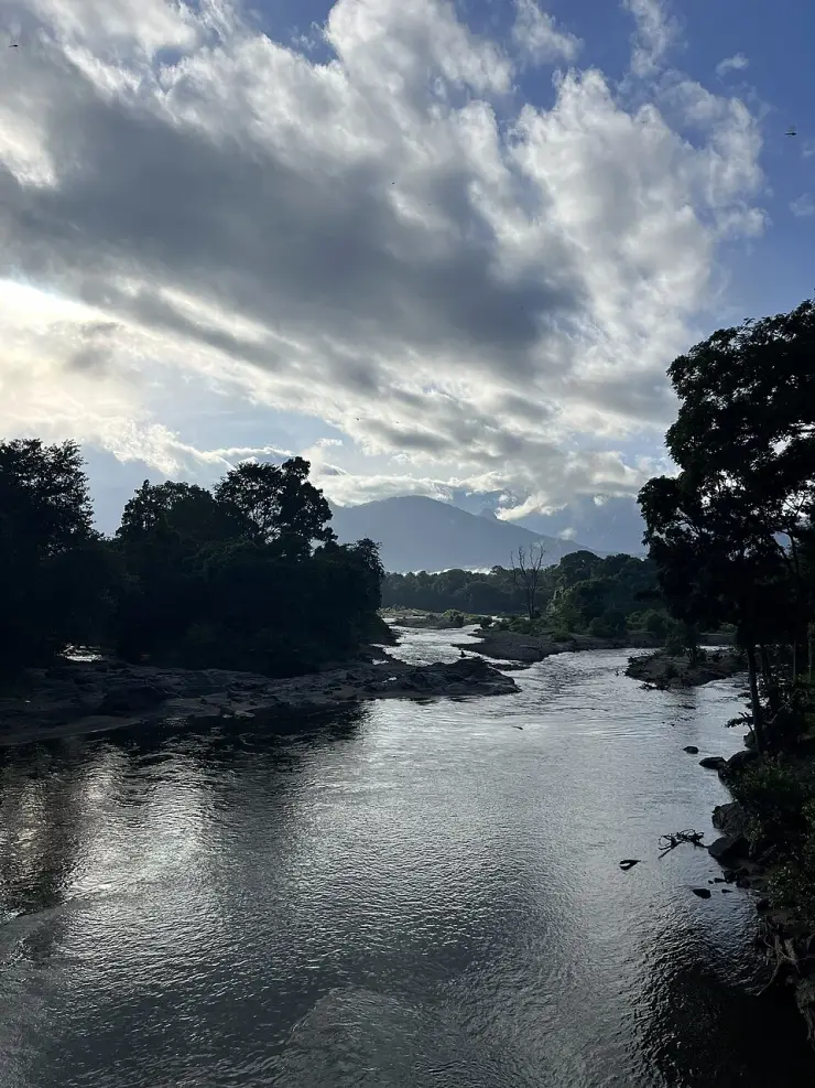 The Karimpuzha flows between wooded banks and exposed rocks below cloud and distant hills at Nedumkayam.