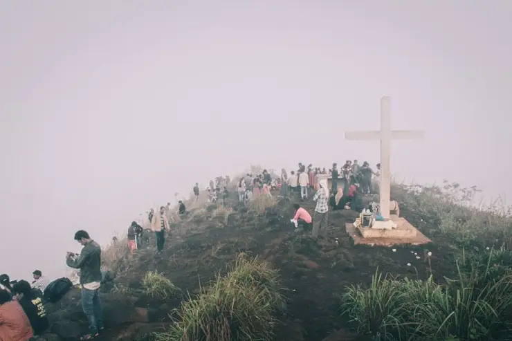 Visitors stand along a mist-covered Kurumbalakotta ridge beside a large white cross.