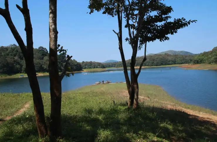 Blue lake water surrounds a grassy, wooded peninsula, with small rafts near the shore.