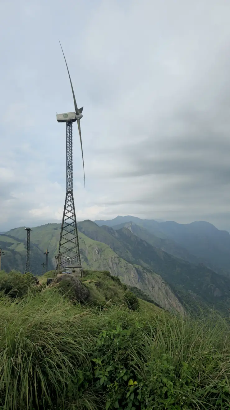 Lattice-tower wind turbine above the grassy Chathurangapara ridge and steep green rock slopes