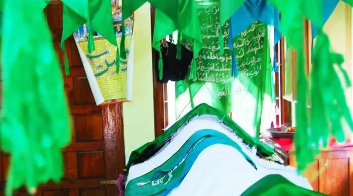 Green fabric hangs around a cloth-covered tomb inside Varambetta’s timber-posted maqaam.
