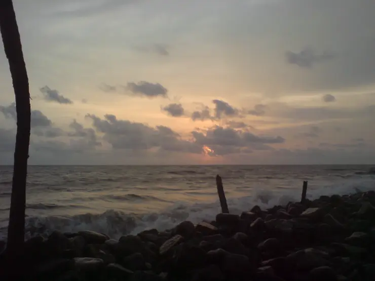The low sun glows above the sea behind dark rock protection on the Nattika coast.