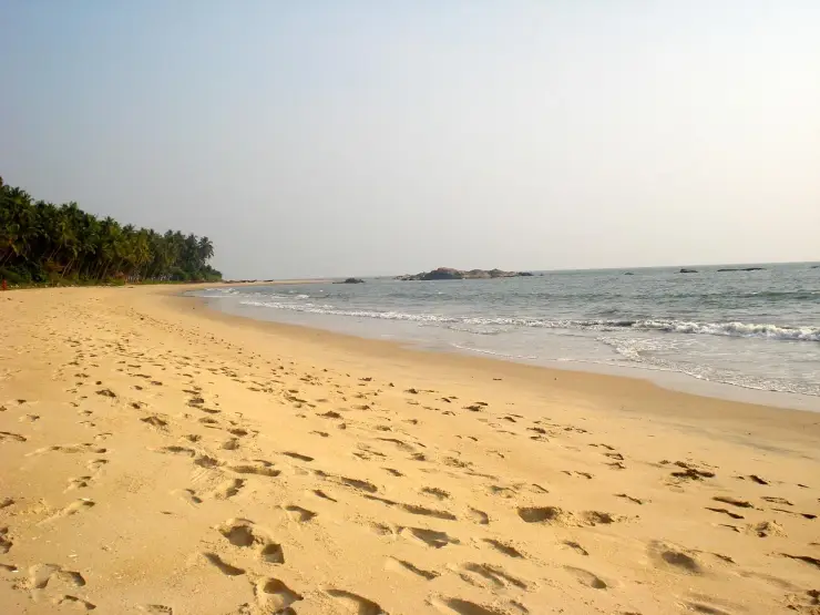 Footprints cross the open sand at Kizhunna, with low dark rocks and the sea beyond.