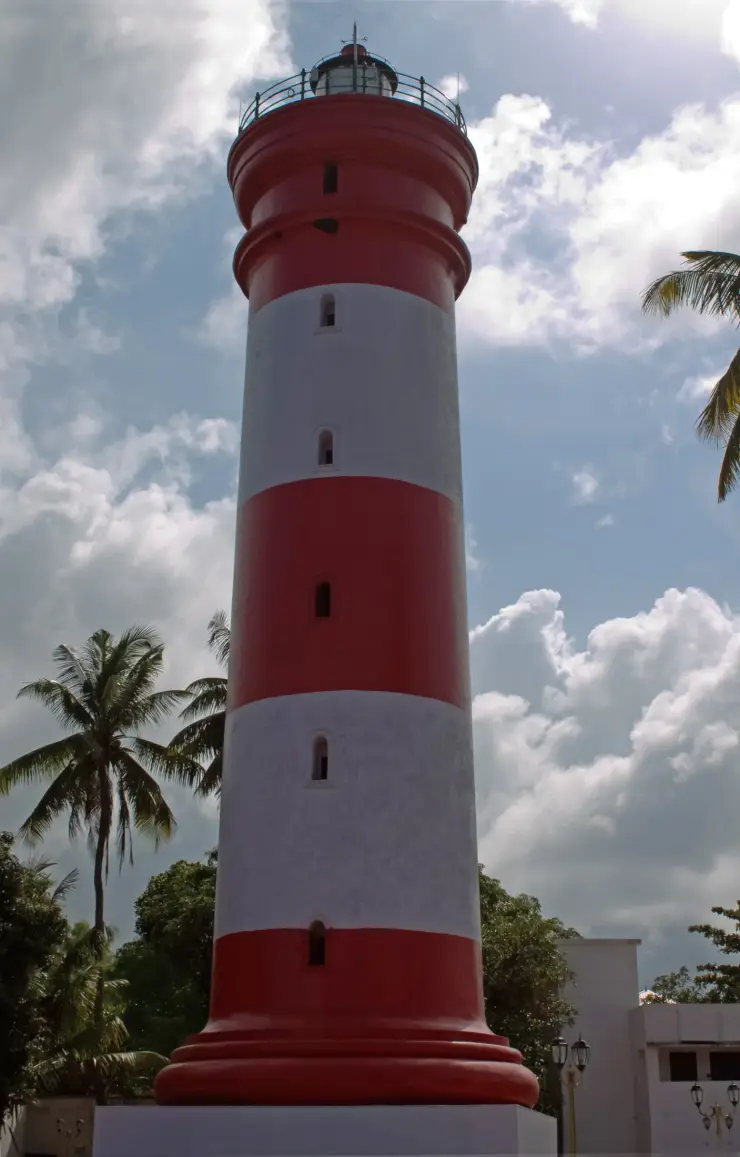 The red-and-white cylindrical lighthouse rises above its base buildings and surrounding palms.