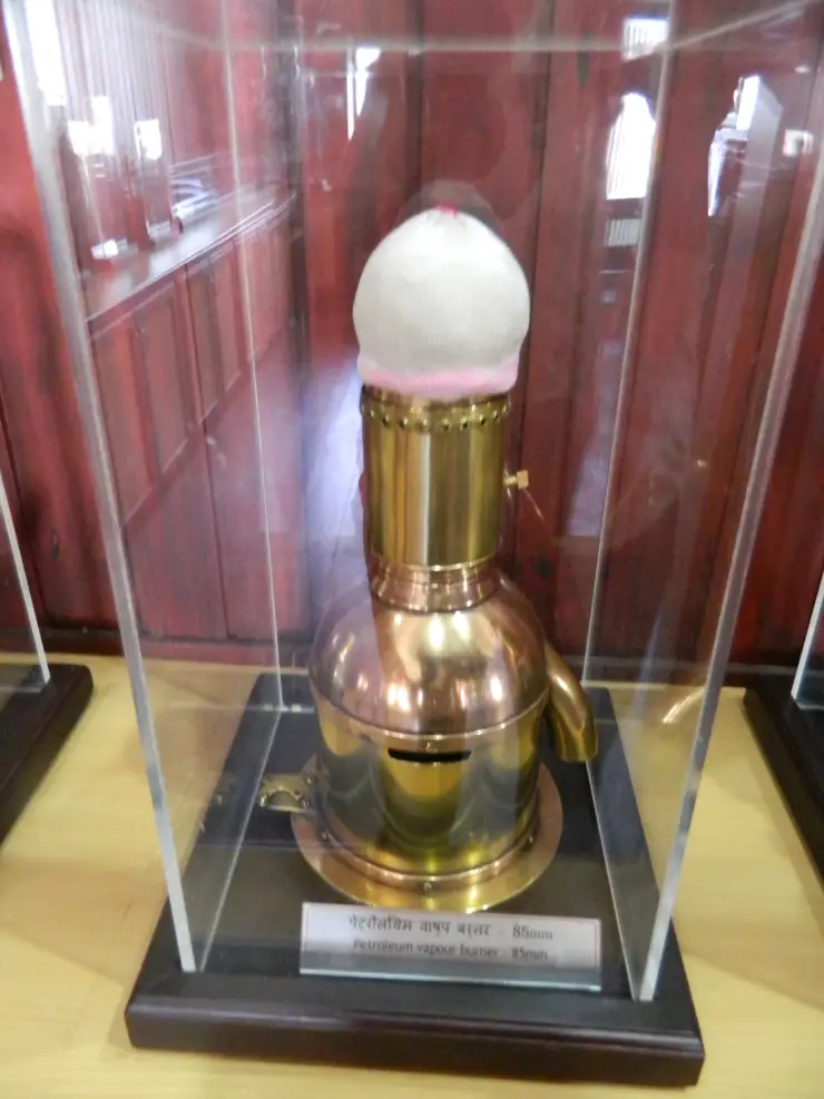 A petroleum-vapour burner with a white mantle stands behind glass beside its identifying museum label.