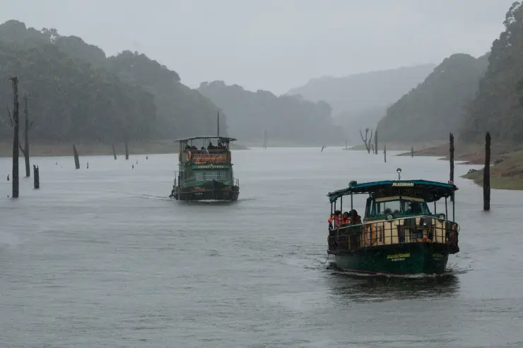 Passengers wear orange lifejackets on a covered Periyar boat during wet weather.