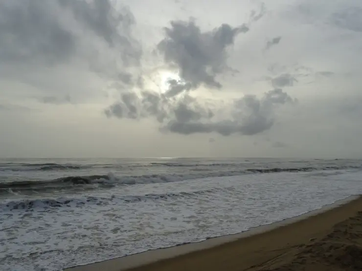 Waves reach a broad sandy shore beneath a cloudy sky at Kanhangad.