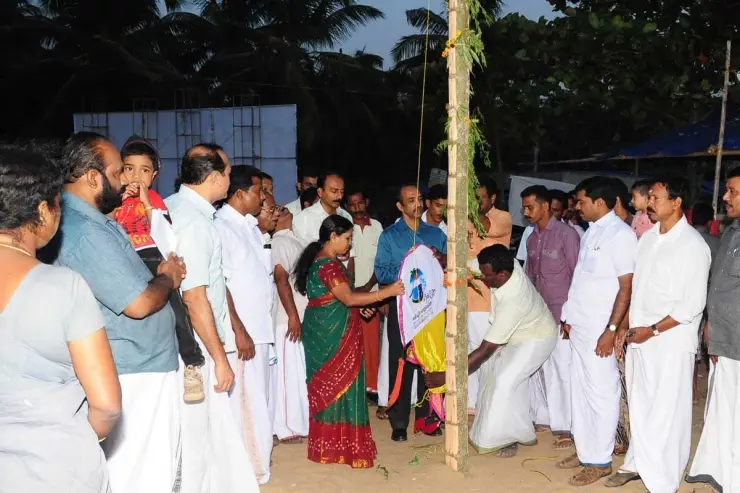 People gather around a decorated flagpole on Nattika’s sand at dusk in an archival festival photograph.