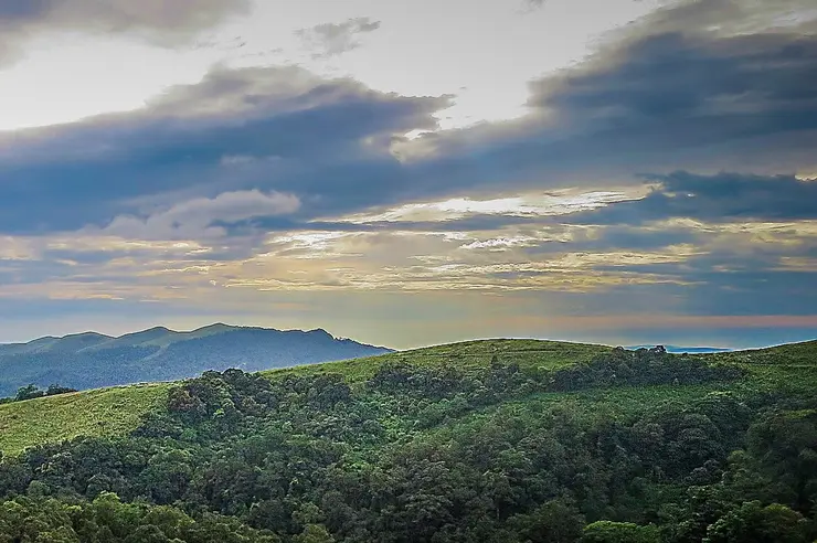 Sunlight breaking through cloud above the grass ridges and forested folds of Gavi