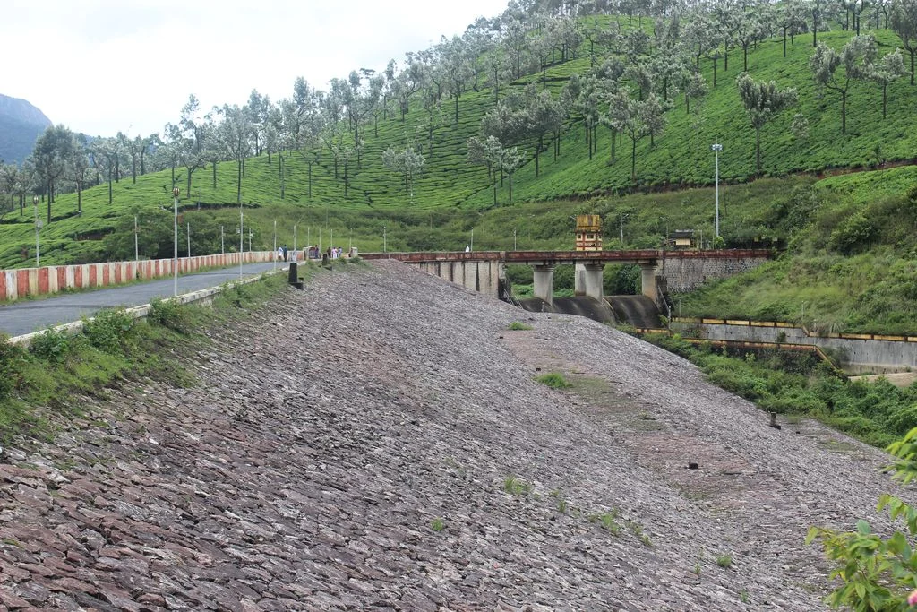 Anayirankal’s stone-covered embankment and adjoining channel below a tea-covered hill.