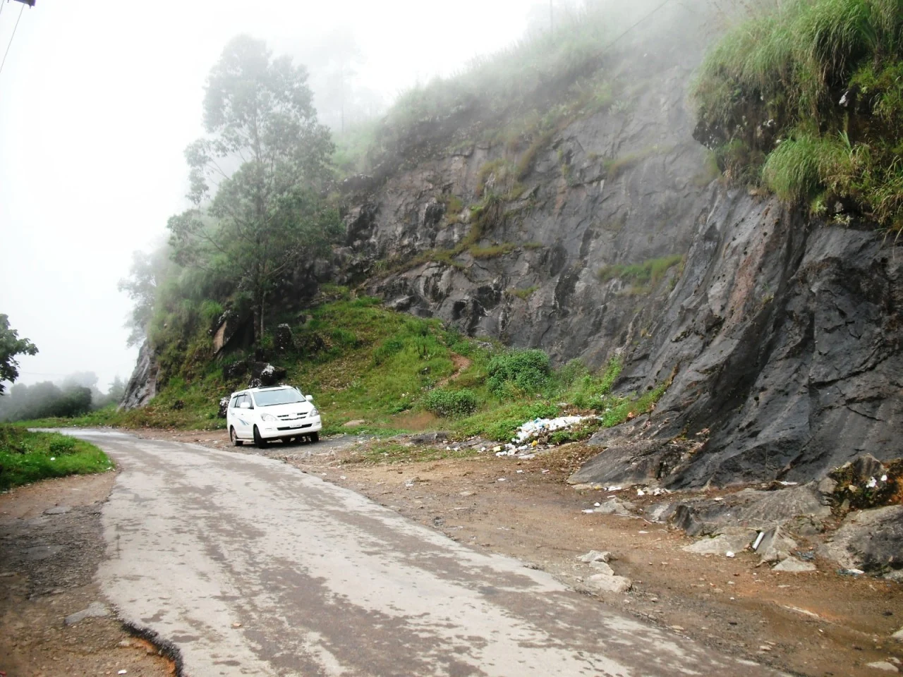 A wet narrow road between a rock-cut bank and vegetation on the Pothamedu approach, in an older photograph.