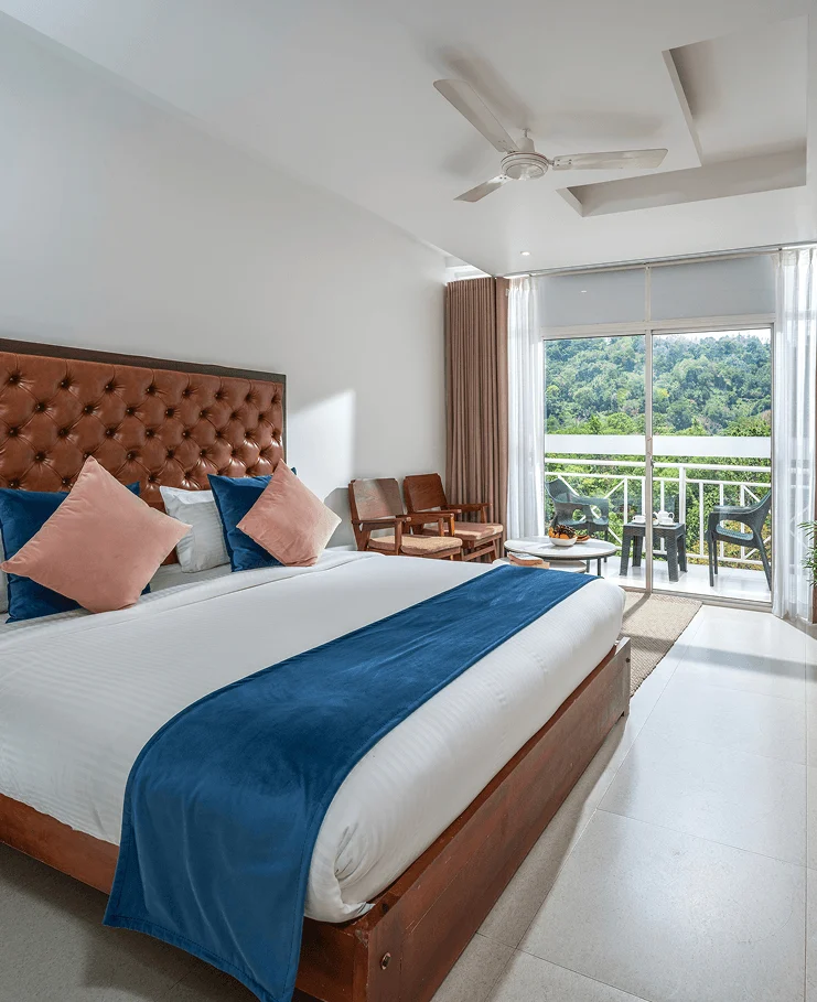 A guest room with a blue bed runner, wooden chairs and a balcony facing greenery at the former Rivulet Resort, now Blanket Riverside.