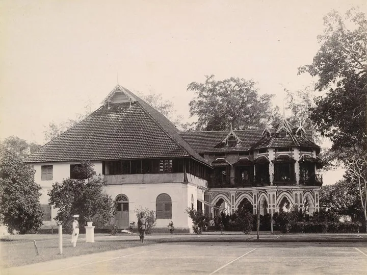 Period photograph of Bolgatty Palace, Kochi, showing the Dutch tiled block and a later ironwork verandah wing, with a tennis court in the foreground