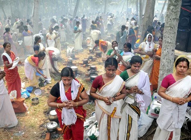 Women cooking pongala offerings in earthen pots amid woodsmoke under coconut palms at the Karikkakom Pongala, Thiruvananthapuram