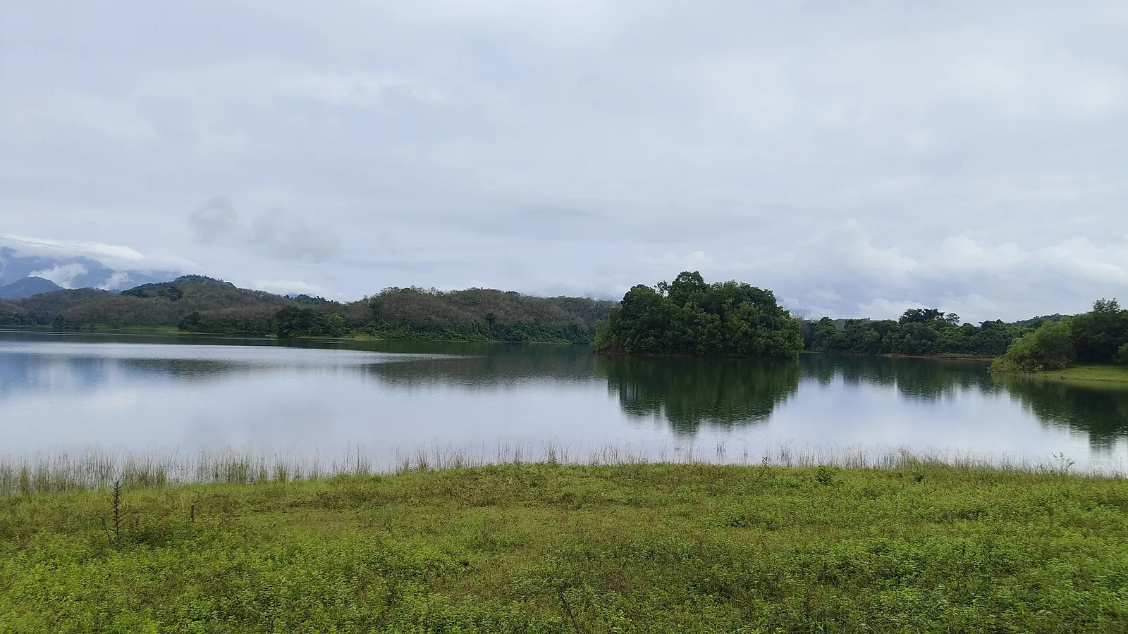 The Peruvannamuzhi reservoir under monsoon cloud, a wooded island at its centre and the Western Ghats receding behind.