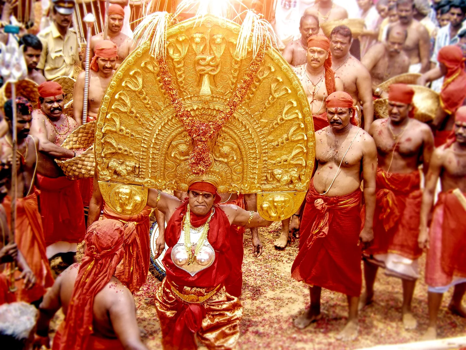 A performer in the golden mudi headdress of the goddess at the Vellayani Kaliyoottu festival, surrounded by attendants in red