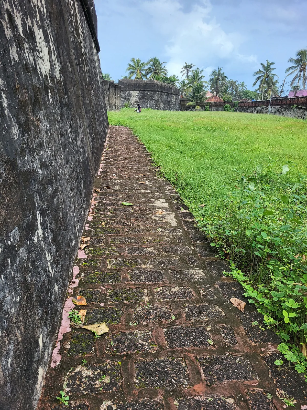 A brick path running along the inside of the laterite rampart at Anchuthengu Fort, with the bastion and green interior beyond