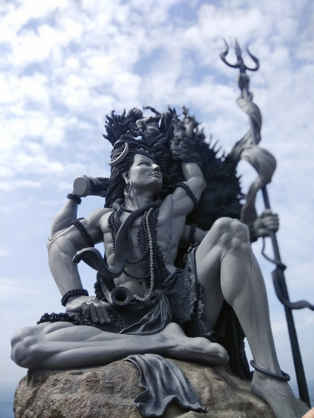 The Gangadhareswara sculpture at Aazhimala seen from below, showing the matted locks holding the small figure of Ganga, the crescent moon and the trishul against the sky