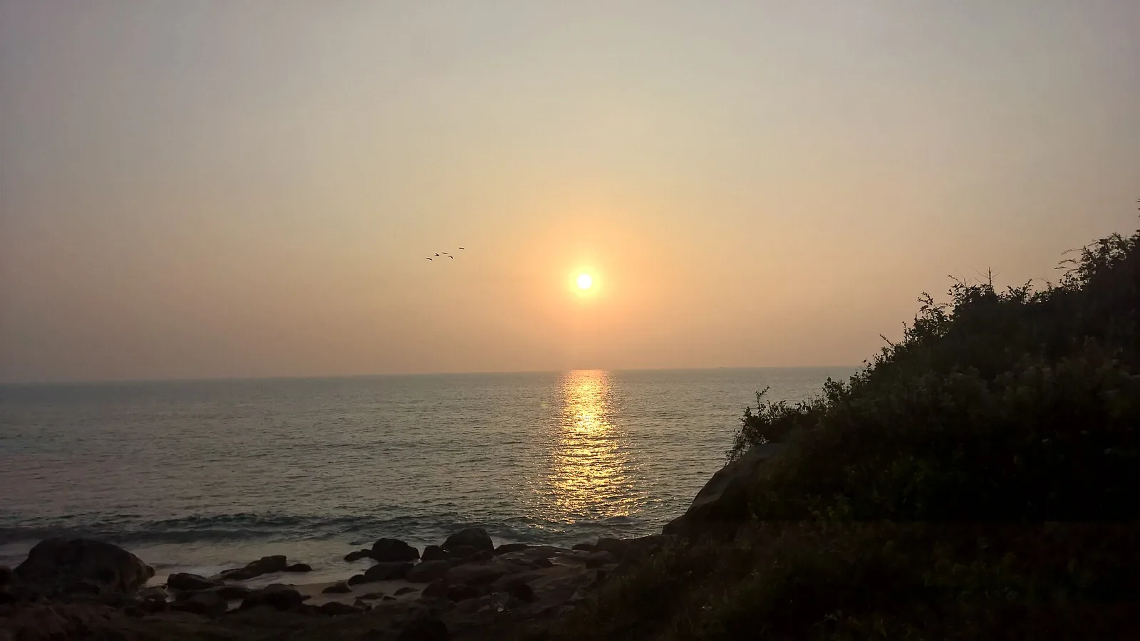 Sunset over the sea at Kovalam, with dark rocks in the foreground