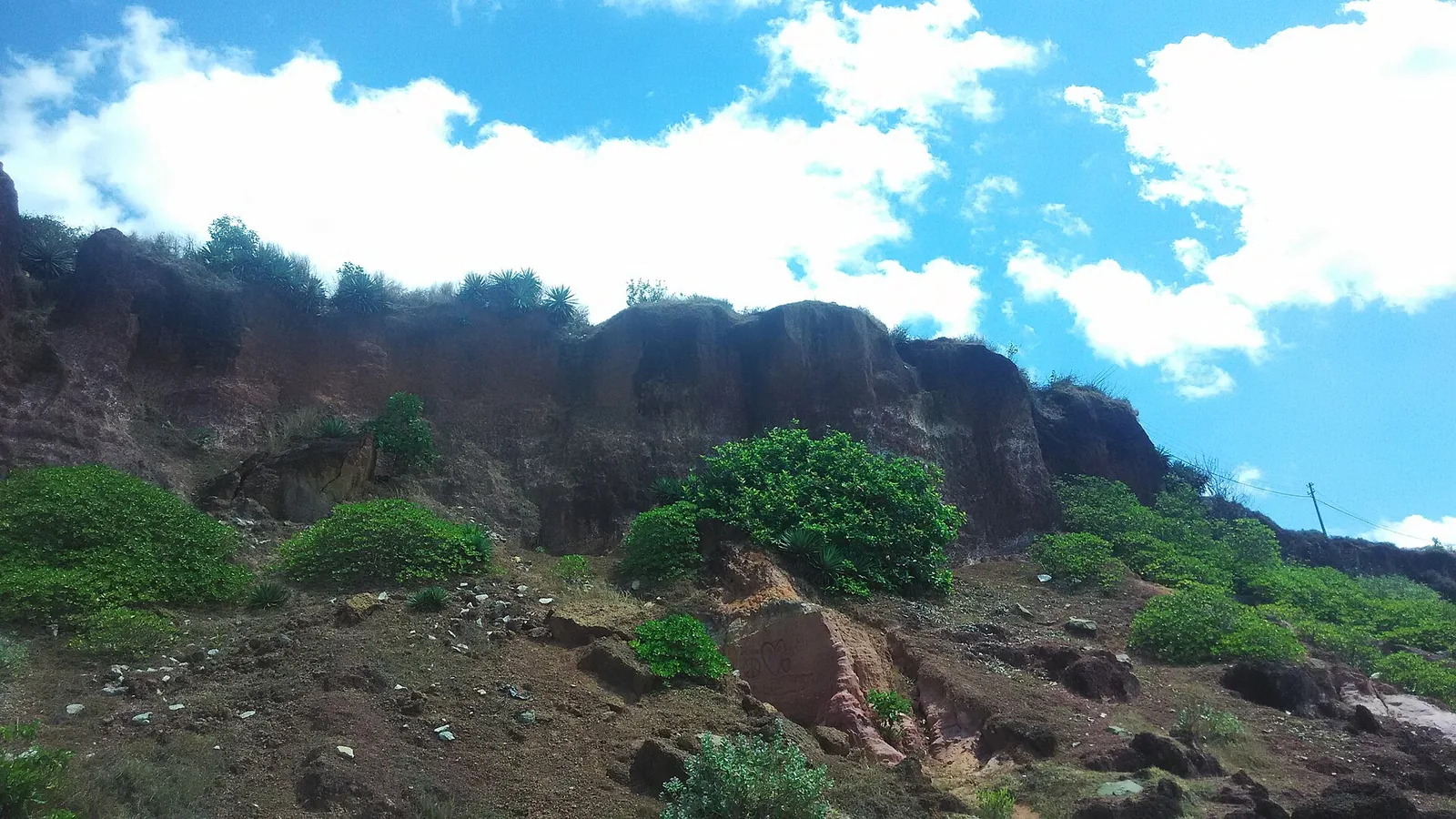 The layered face of the Varkala cliff seen from the beach, red laterite over paler sandstone with slumped material at the base