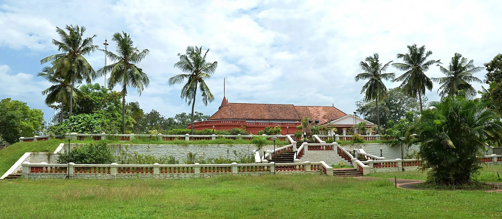 Kanakakunnu Palace seen across its terraced lawns and balustraded retaining wall, with coconut palms around the tiled roof