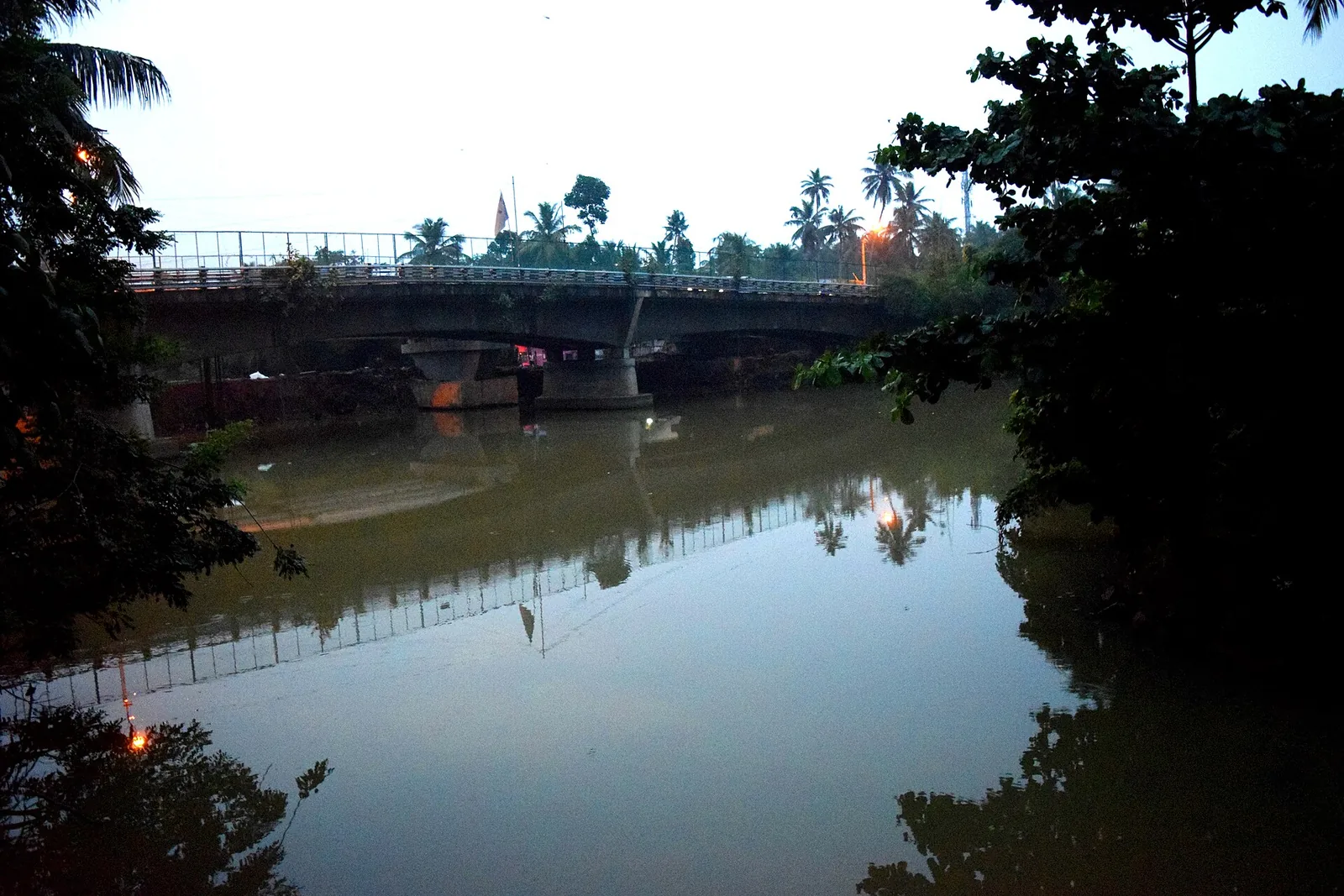 The Karamana river at dusk near the Thiruvallam Parasurama temple, with a road bridge crossing and palms reflected in still water