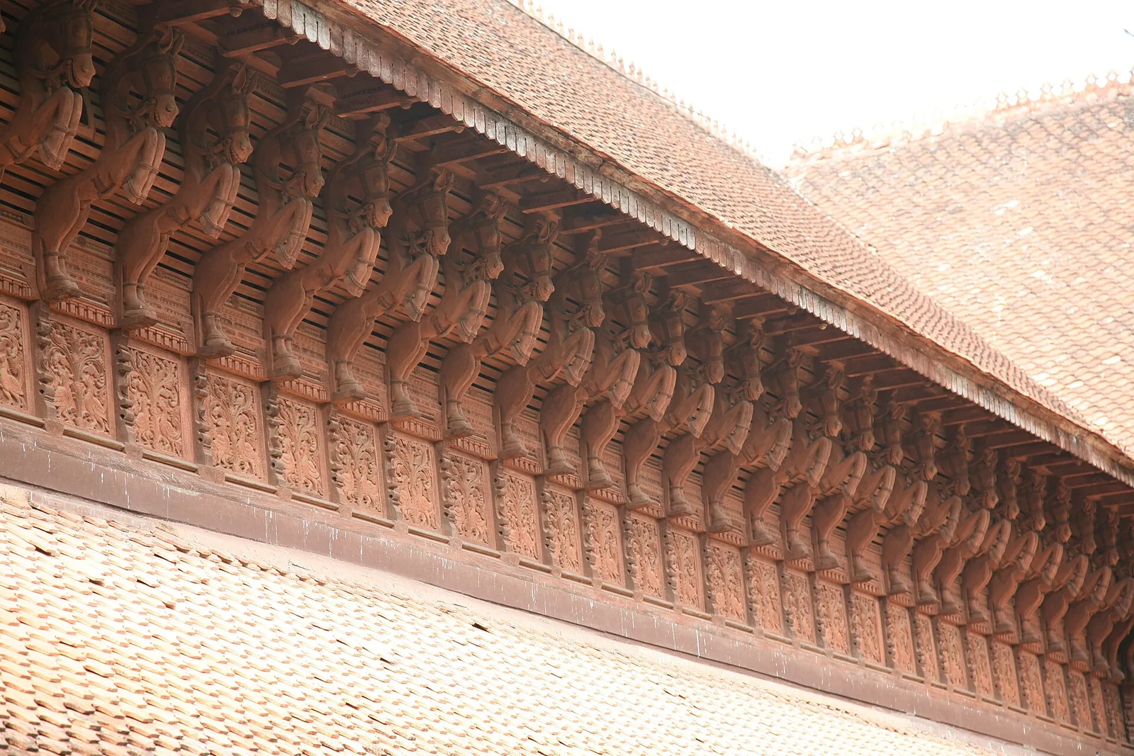 A long row of carved wooden horse brackets under the tiled eaves of Kuthiramalika palace