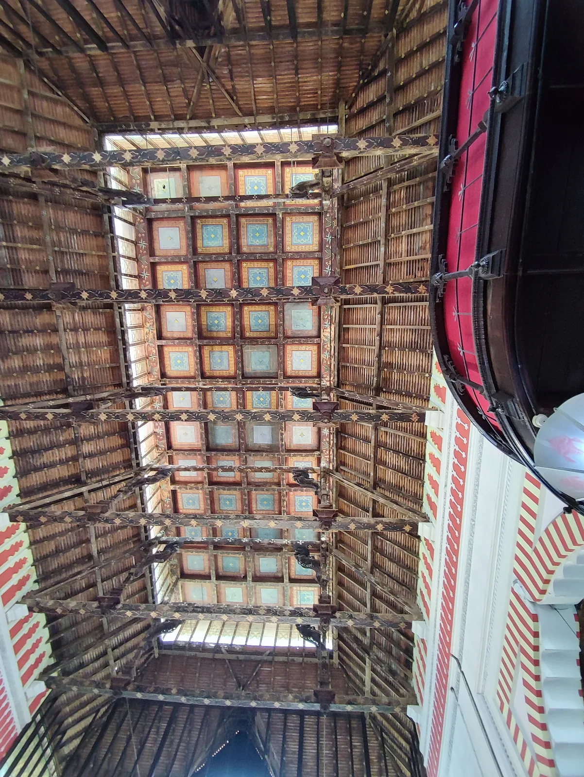 Looking up inside the Napier Museum at the painted coffered ceiling and the open timber roof structure above it, with clerestory light entering at the sides