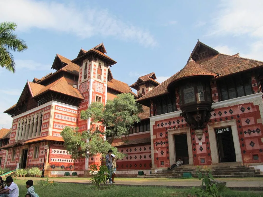 The polychrome exterior of the Napier Museum with its gabled tiled roofs and red, black and cream banding, seen across the lawns of the museum complex