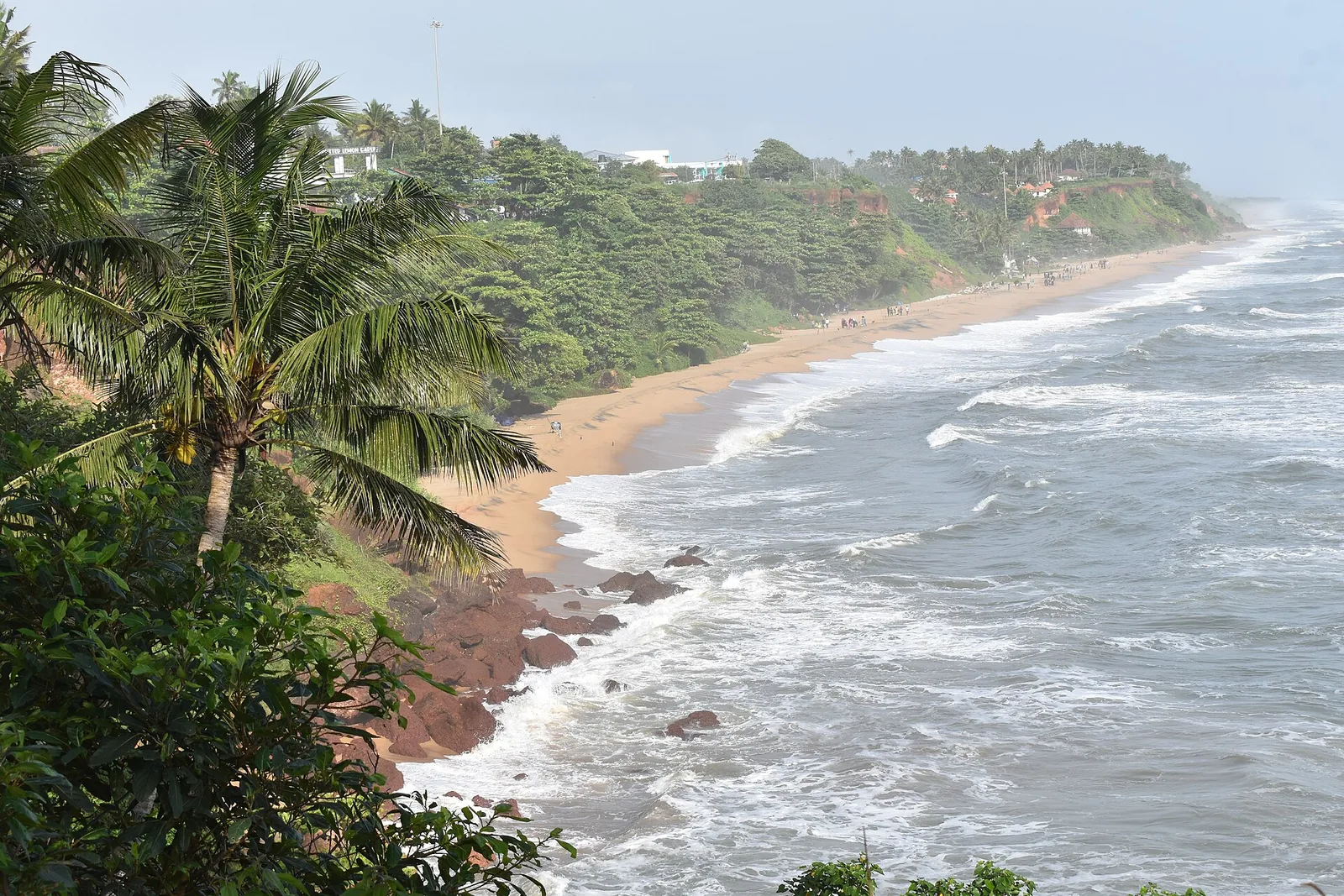 The Varkala cliff coast, red laterite exposed above the beach and boulders at the waterline
