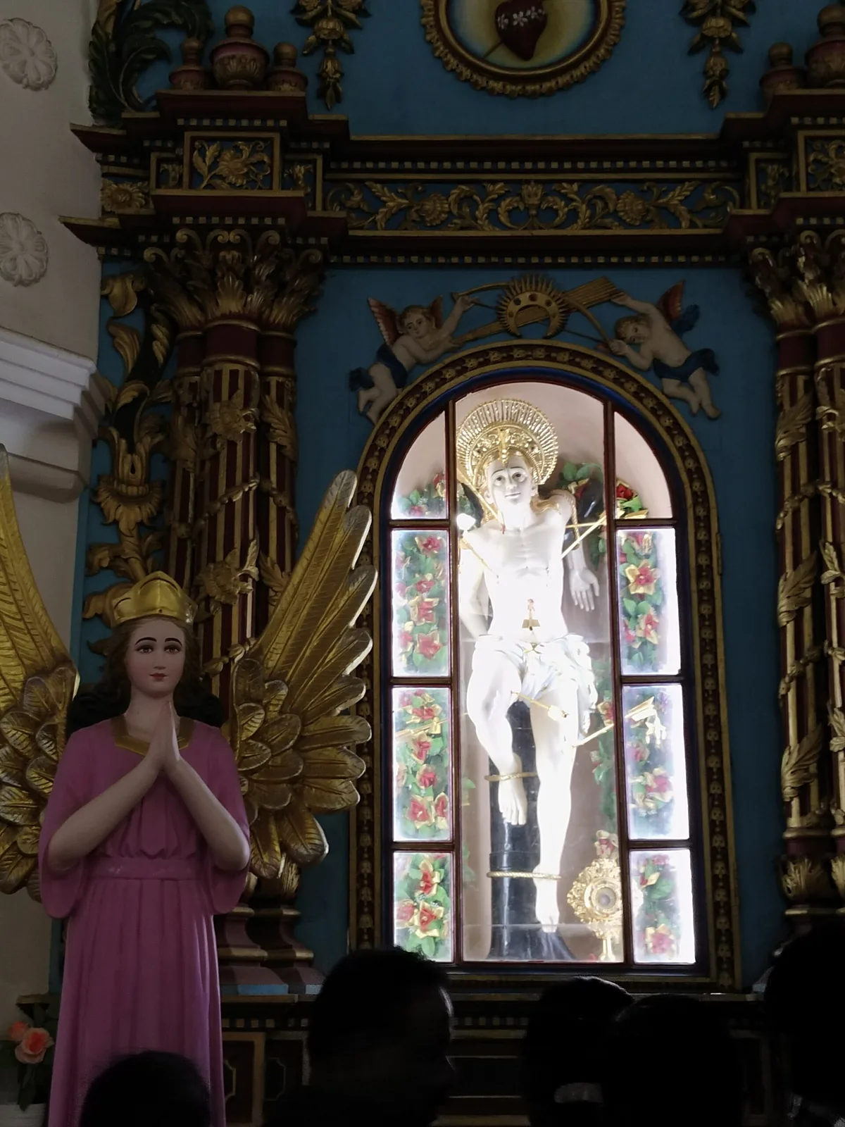 The white statue of St Sebastian bound to a dark post and pierced with gilt arrows, inside a glazed arched case set in a carved and gilded baroque reredos on a deep teal ground