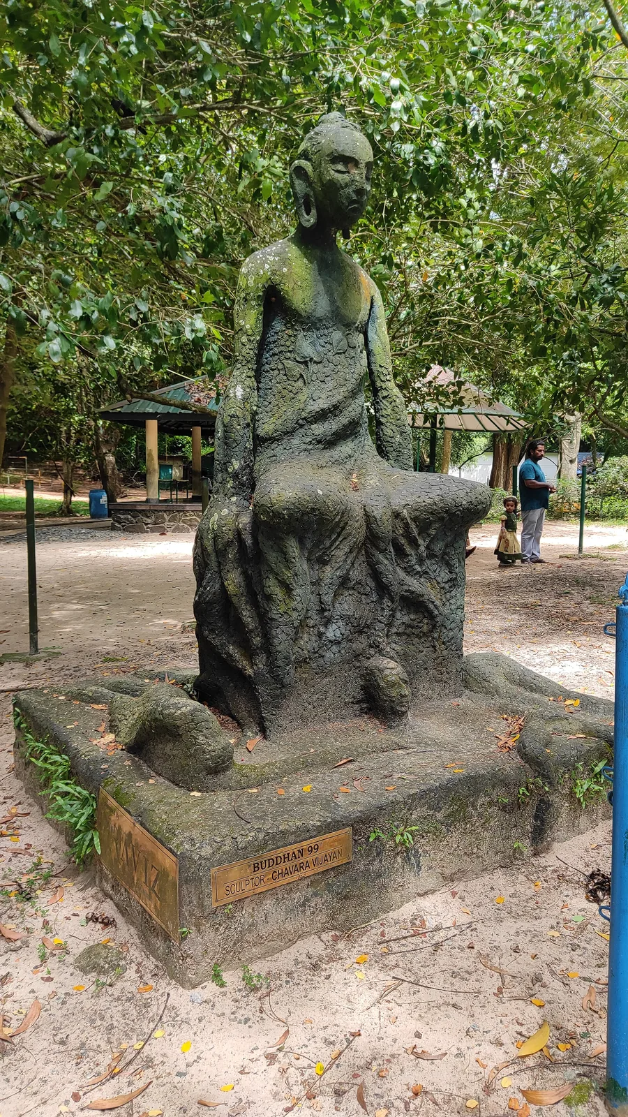 A contemporary sculpture titled Buddha 99 standing on open ground among trees in the Asramam park at Kollam