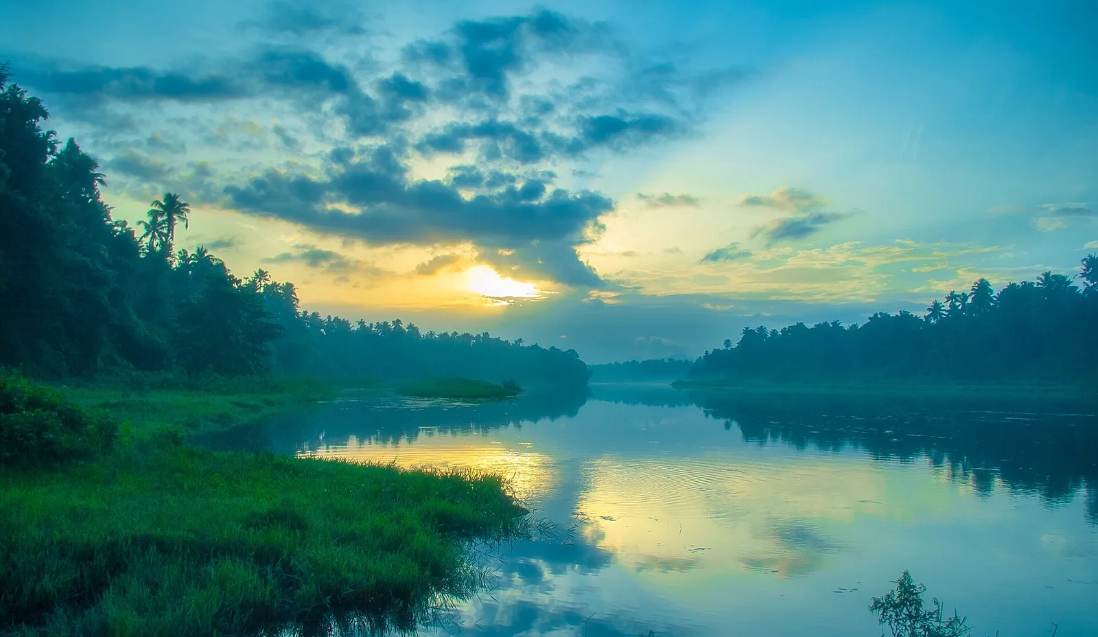 A broad still reach of the Chalakudy river at sunrise, palms silhouetted on both banks and a low grassy islet mid-stream